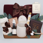 Wildflower Pop Ruby Spa Box with Burgundy blanket, bath salts, bath bomb, linen mist, cream socks, tea sampler, and mini honey and dipper. On light grey background 