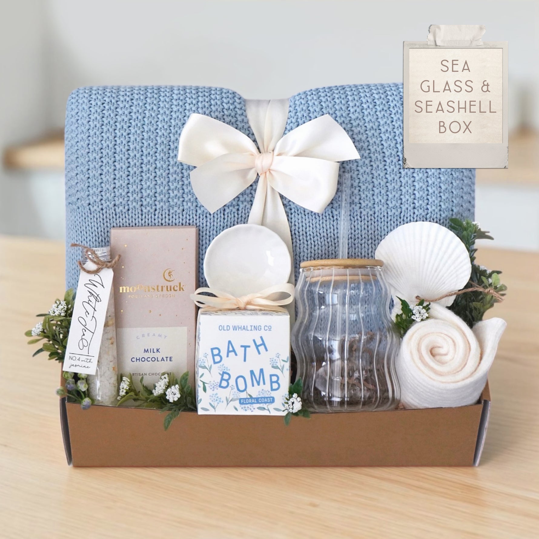 Ocean-inspired self-care gift set with cozy blanket, glass tumbler, knit socks, seashell ornament, and spa essentials.