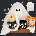 Halloween-themed gift set with ghost pillow, pumpkin, Wildflower Pop Ghost mug, and candy on a dark background.