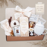 Golden Autumn blanket gift basket with tea, candles, and other items on a gray background