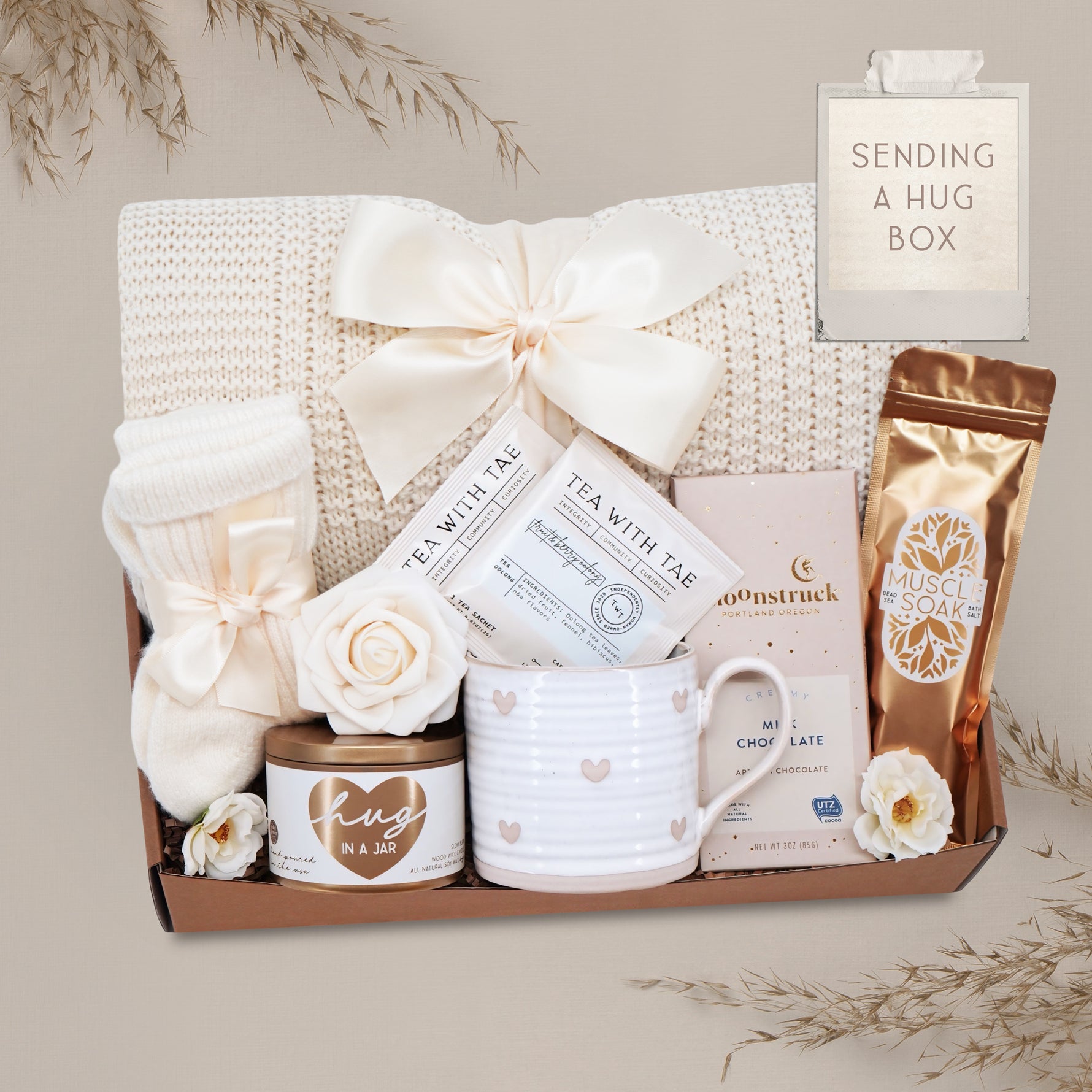 Wildflower Pop Sending a Hug Blanket gift box, with cream lace knit blanket, tea sampler, cream knit socks, hug in a jar soy wax candle, Wildflower Pop Heart ceramic mug, Moonstruck Milk Chocolate bar, and muscle soak
