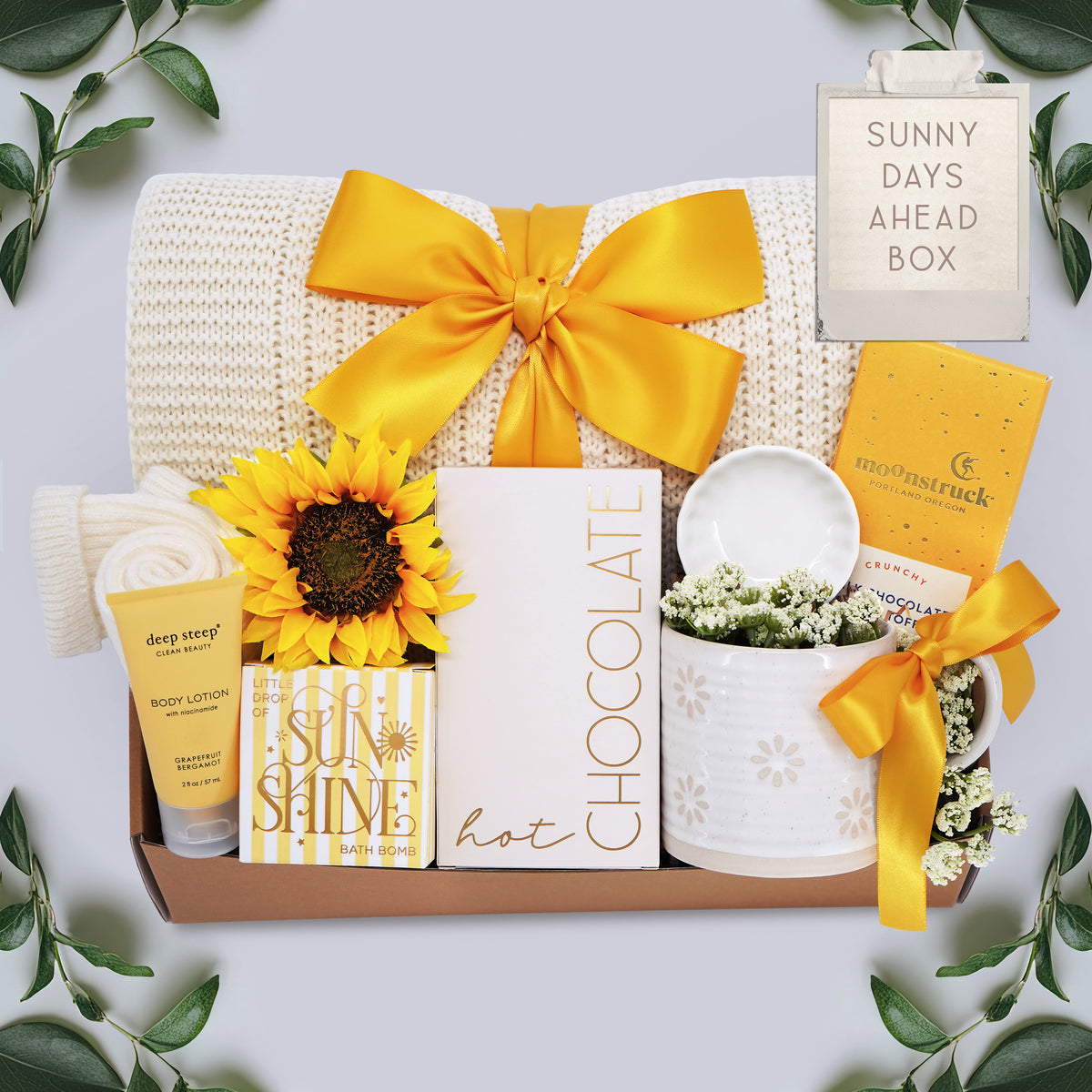 Wildflower Pop Sunny Days Ahead blanket gift box with a cream lace knit blanket, Wildflower Pop daisy ceramic mug, scallop trinket dish, moonstruck milk chocolate and toffee bar, little drop of sunshine bath bomb, faux sunflower, deep steep lotion, and cream knit socks