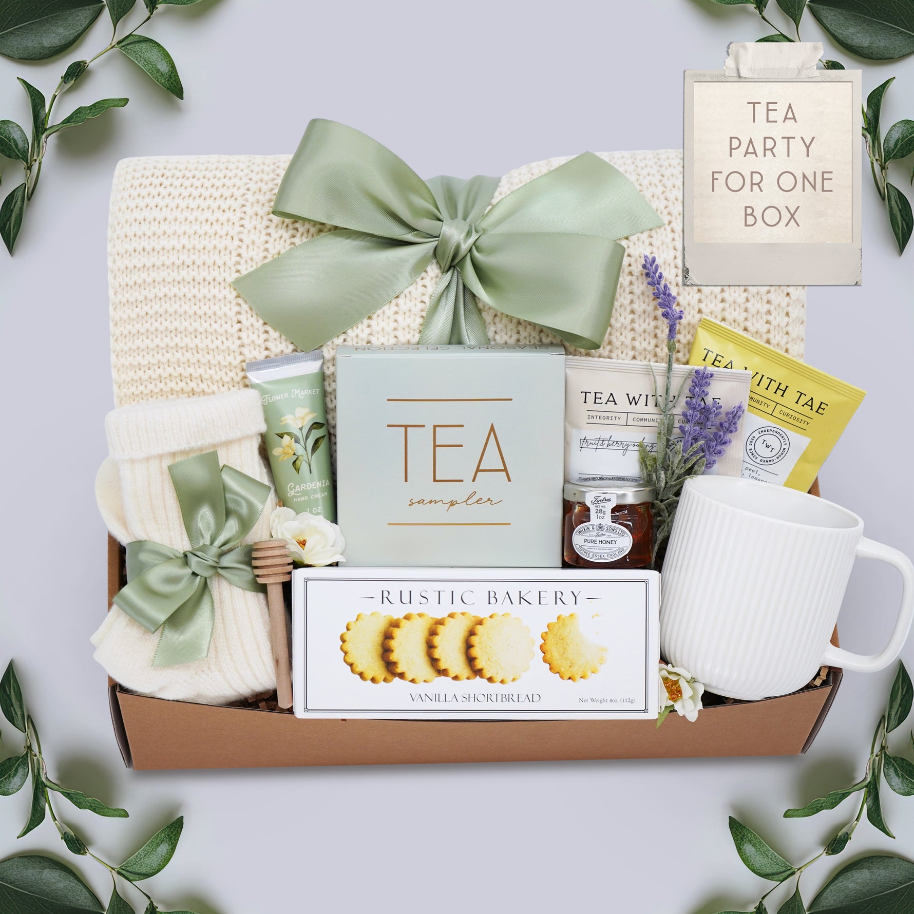 Wildflower Pop Tea Party for One comes with a cream lace knit blanket, cream knit socks, Flower Market Gardenia hand cream, Tea Sampler, Rustic Bakery shortbread cookies, ribbed white ceramic mug, mini honey and dipper