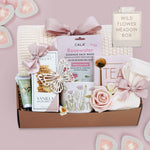 Wildflower Pop wildflower meadow blanket gift box with a cream lace knit blanket, Rosewater face mask, gold spoon, tea sampler, cream knit socks, faux rose, wildflower ceramic mug, wood butterfly ornament, Rustic bakery vanilla shortbread, Flower Market gardenia hand lotion 