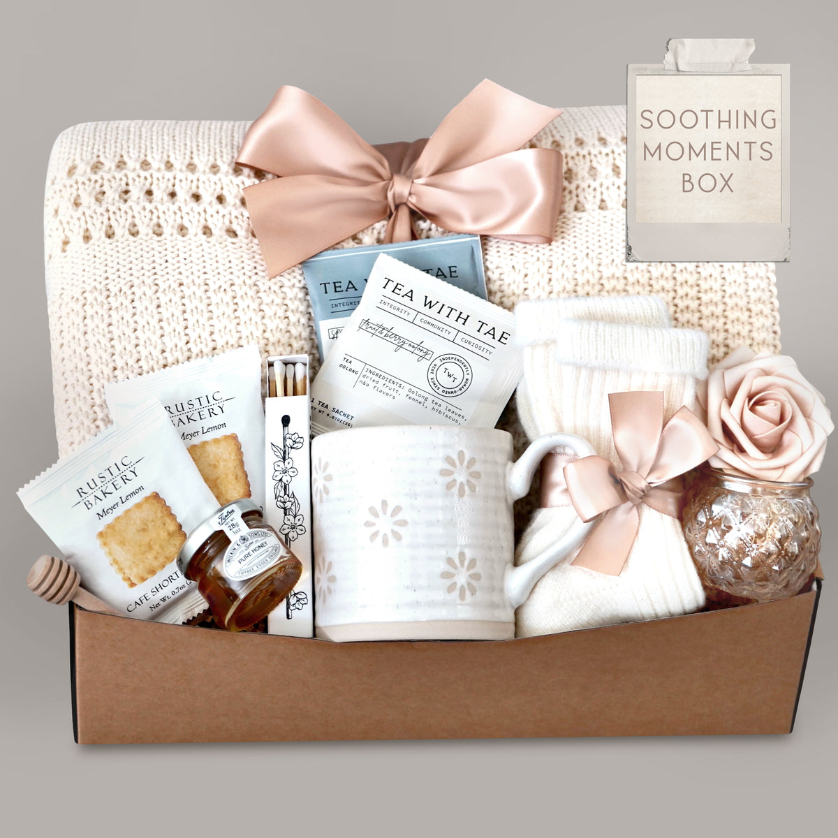 Gift box labeled 'Soothing Moments Box' with tea, cookies, and decorative items on a gray background