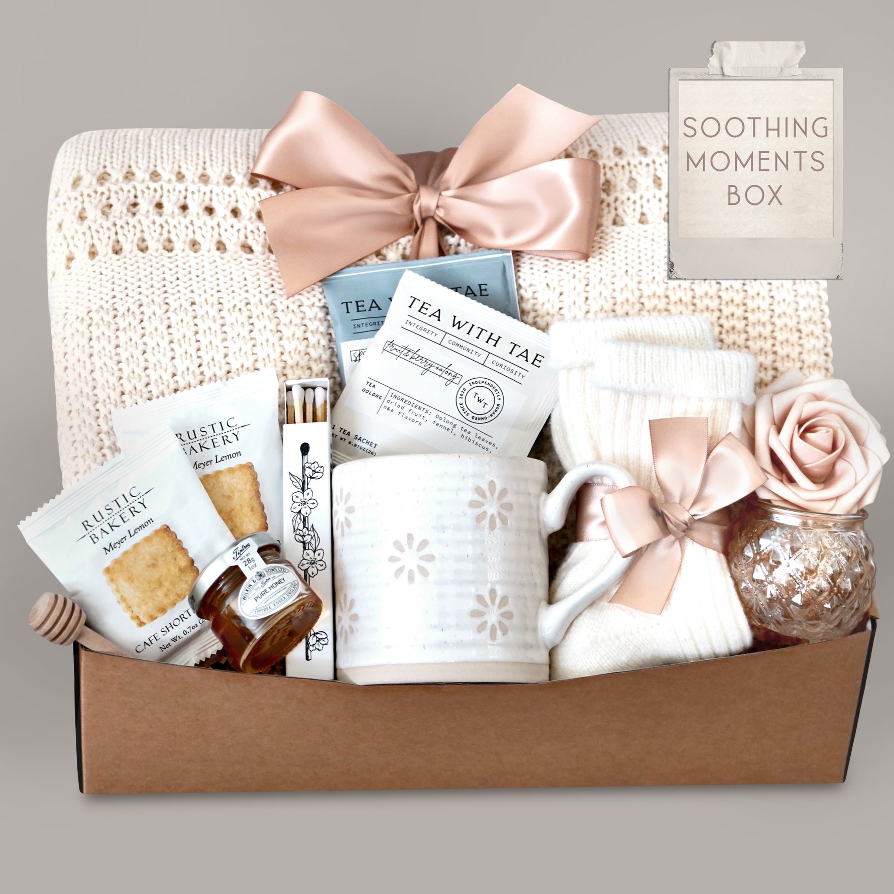 Gift box labeled 'Soothing Moments Box' with tea, cookies, and decorative items on a gray background