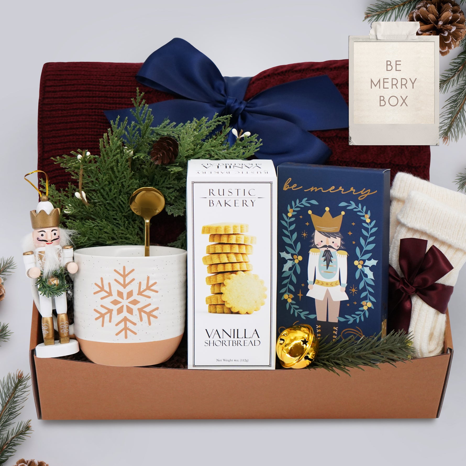 Gift box with festive items including a mug, cookies, and decorative elements on a white background.