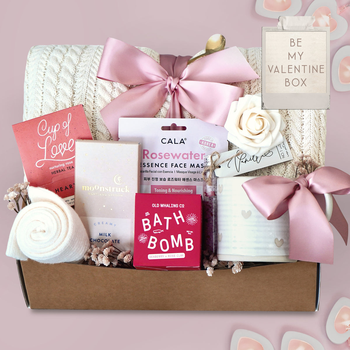 Wildflower Pop Gift box with cable knit blanket,  bath products including a bath bomb, face mask, and tea on a pink background.