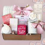 Wildflower Pop Gift box with cable knit blanket,  bath products including a bath bomb, face mask, and tea on a pink background.