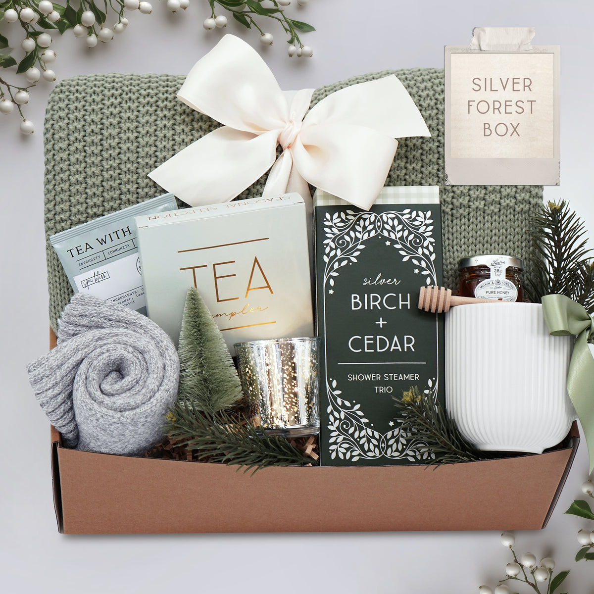Wildflower Pop Silver Forest Blanket gift box, with sage green lace knit blanket, cream ribbed ceramic mug, grey cozy boot socks, silver votive and tea light, mini honey and dipper, silver birch and cedar shower steamers, and tea sampler