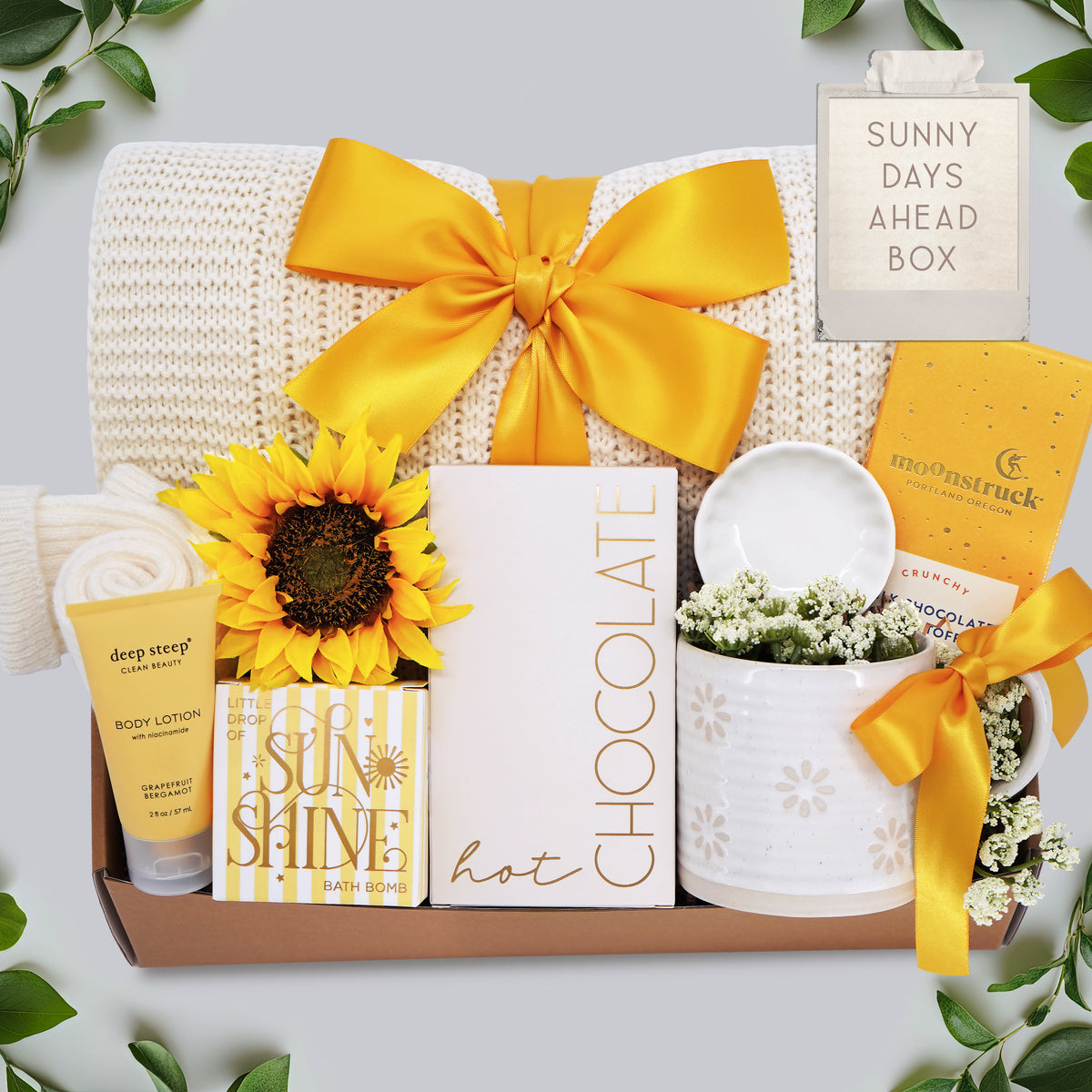 Gift box with sunflower, chocolate bar, and other items on a light background