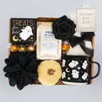 Spooky themed gift box with black roses, mug, and other items on a light gray background