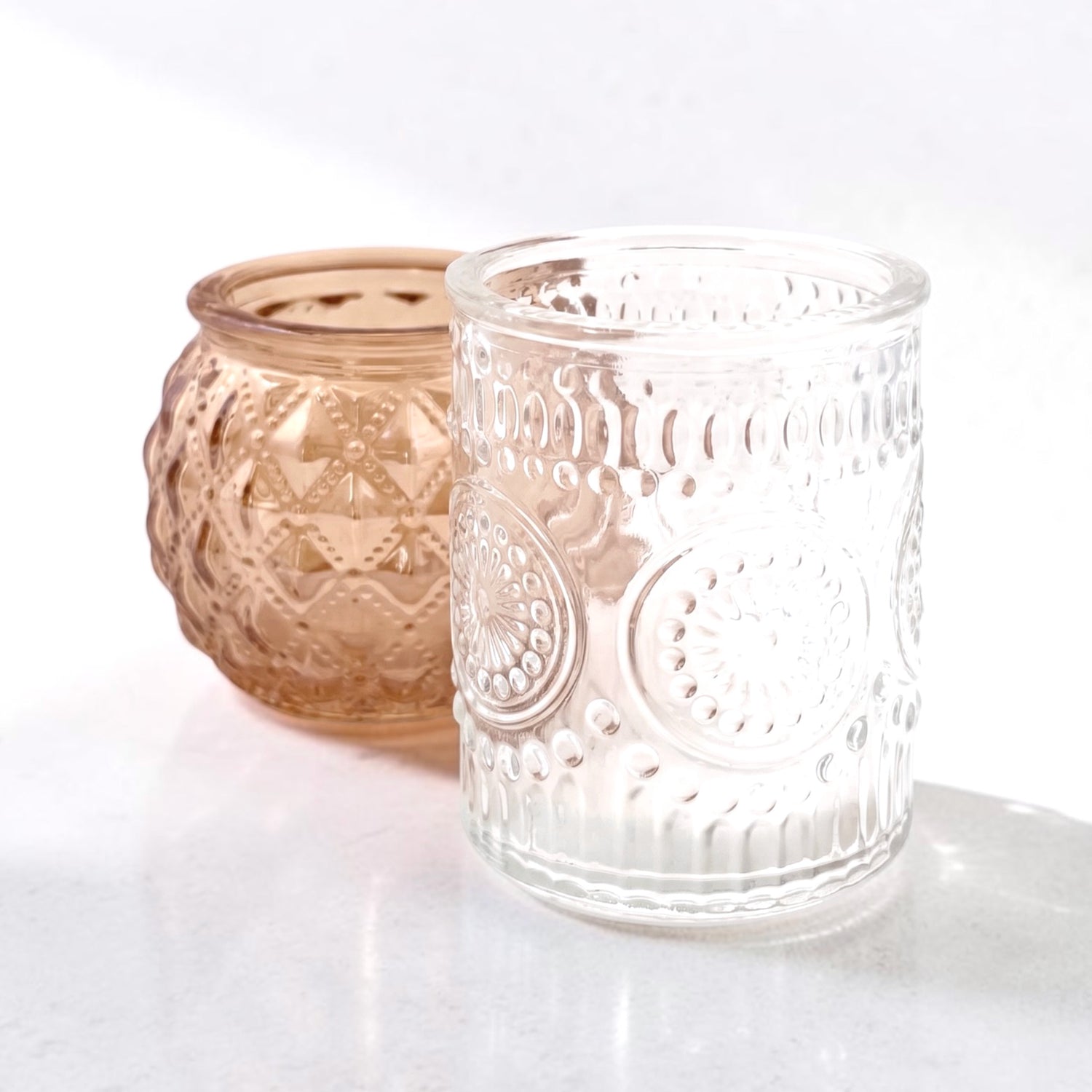 Clear glass votive and rose gold votive on a grey surface 