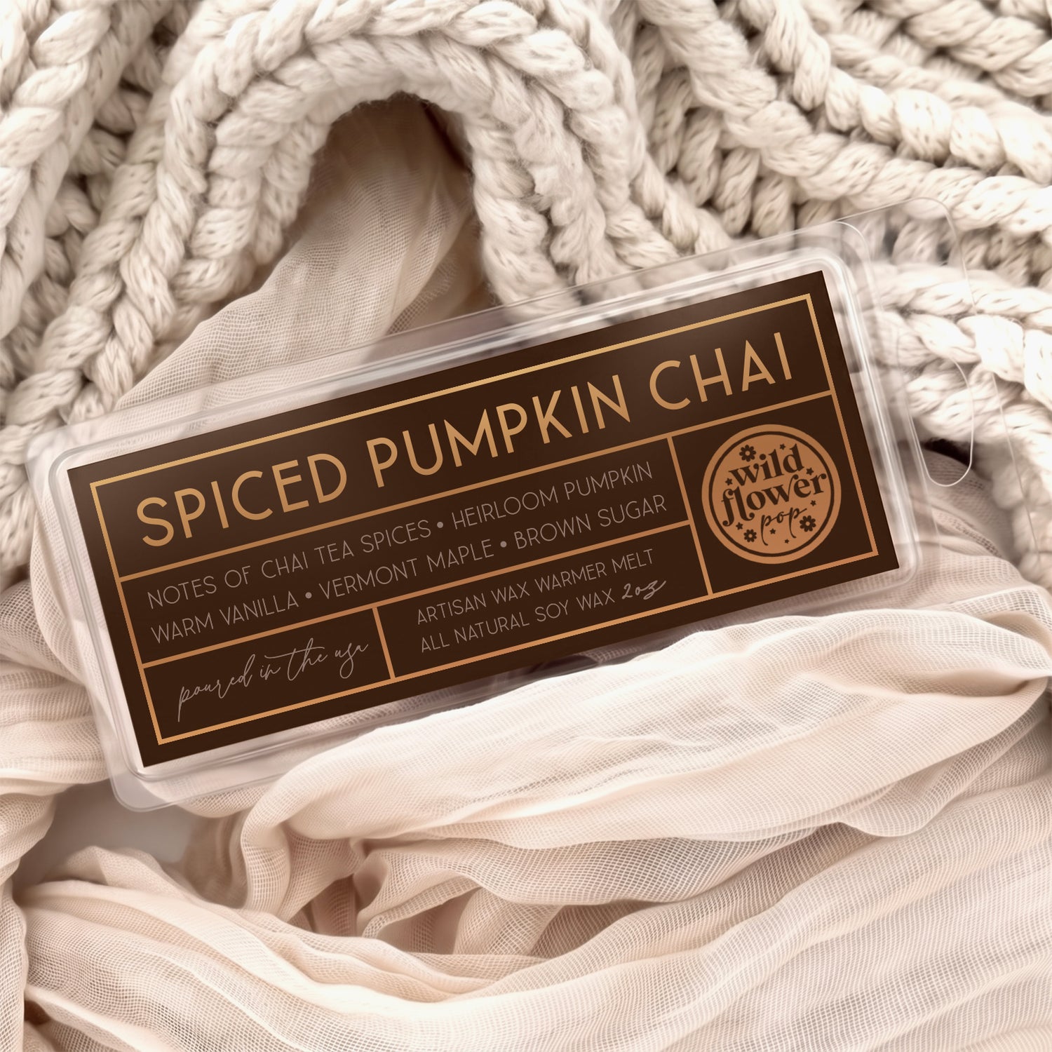 Spiced Pumpkin Chai artisan wax melts, featuring a dark brown label with gold foil, resting on a cozy background of cream-colored softly draped fabric.