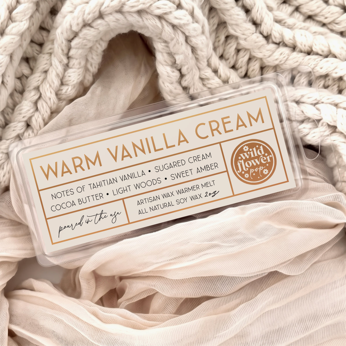 Warm Vanilla Cream artisan wax melts, featuring a cream label with gold foil, resting on a cozy background of cream-colored softly draped fabric.