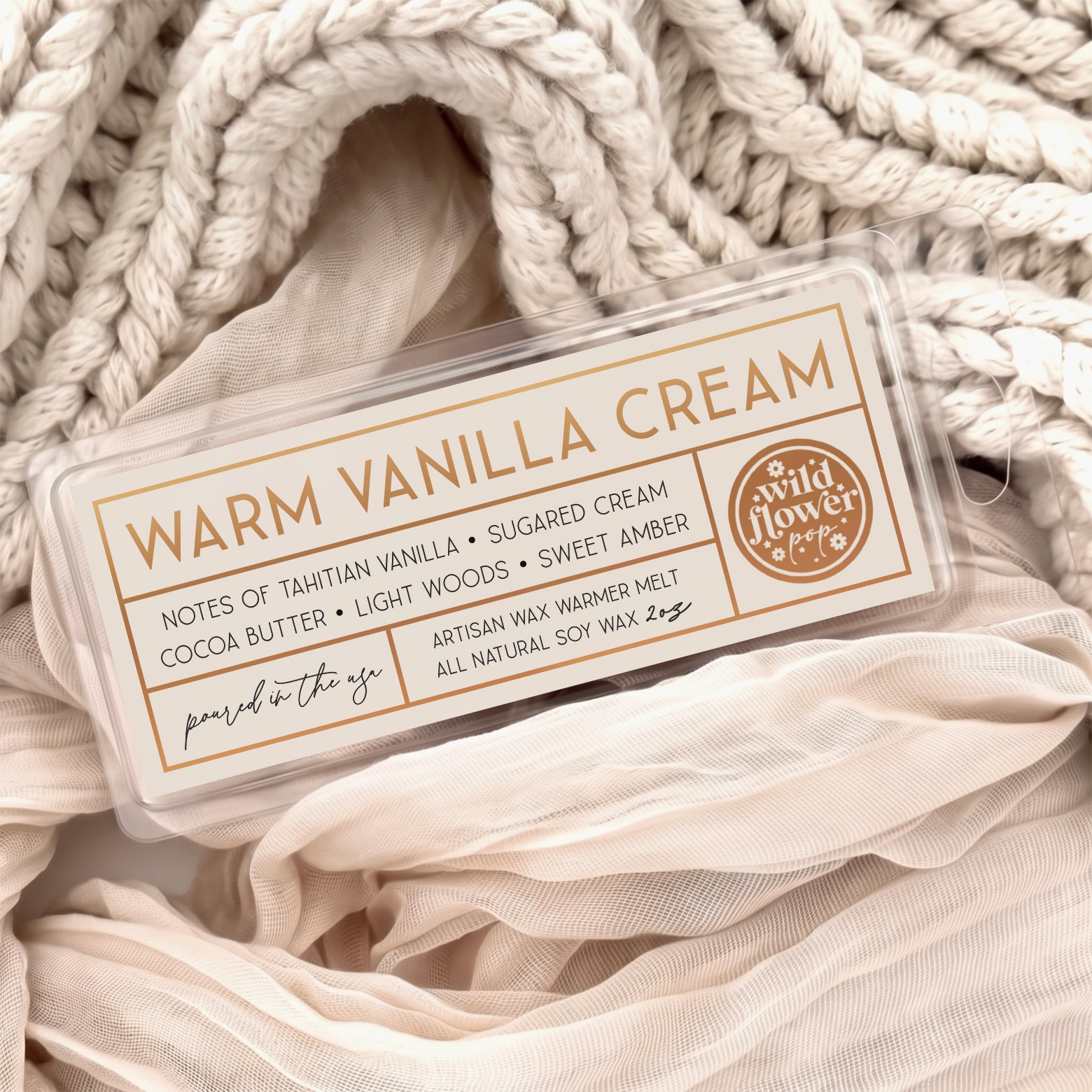 Warm Vanilla Cream artisan wax melts, featuring a cream label with gold foil, resting on a cozy background of cream-colored softly draped fabric.