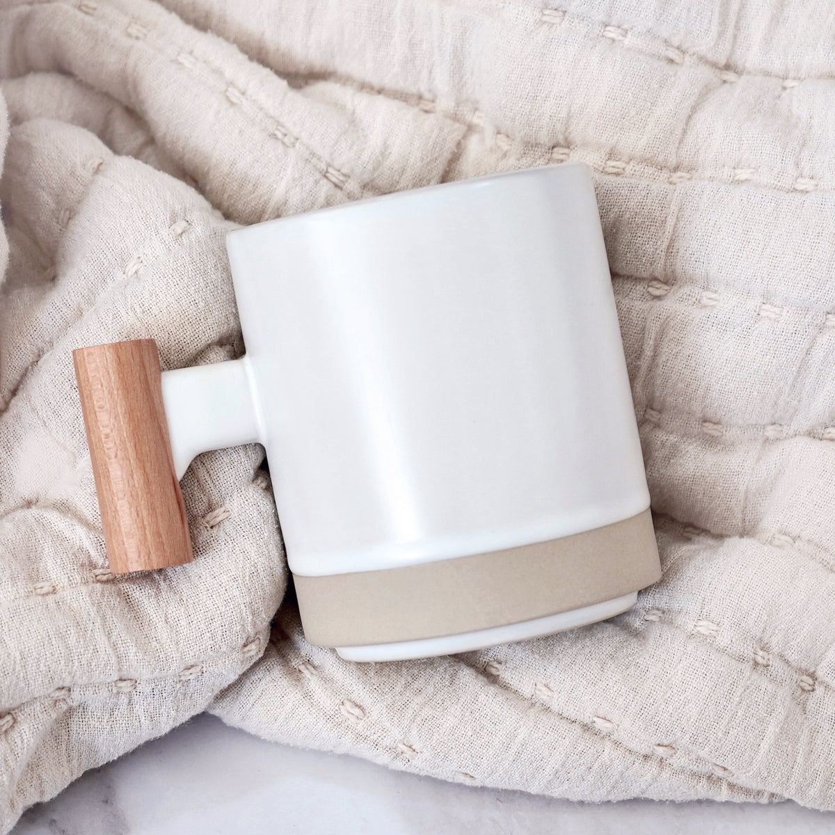 White mug with a wooden handle on a textured beige surface